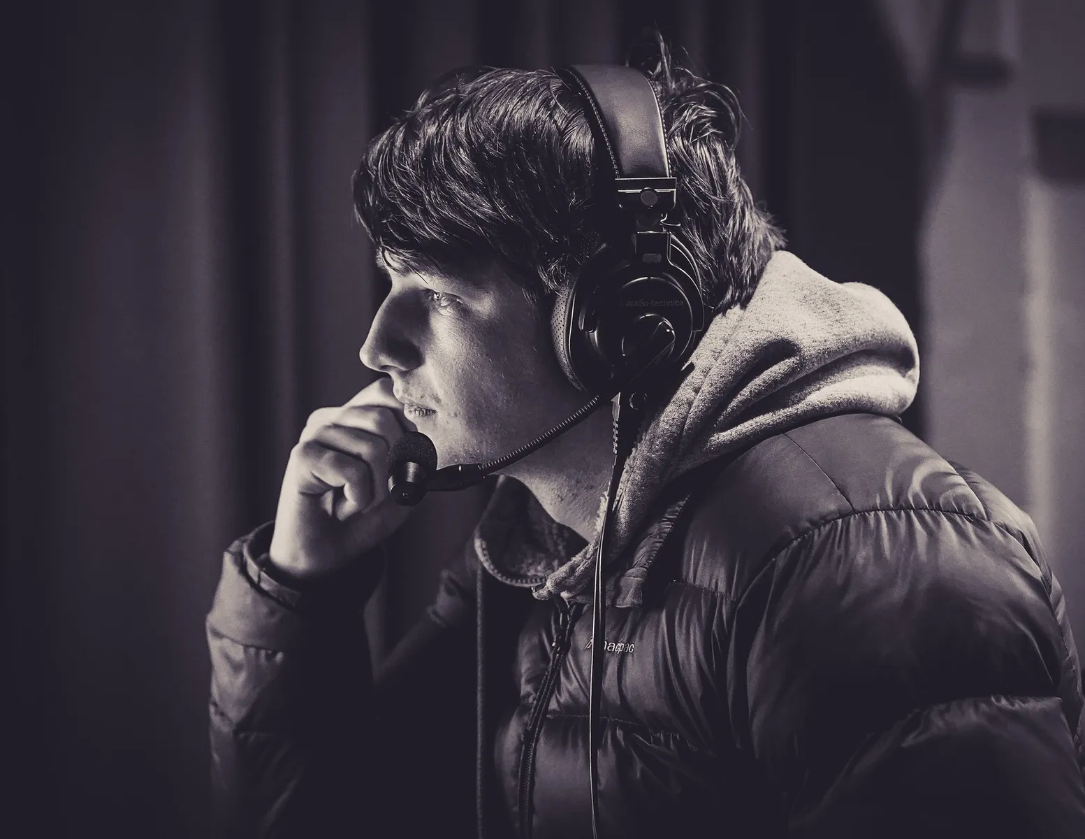 A black and white photo of Ewan Lyon with broadcast headphones on looking at a monitor off screen.